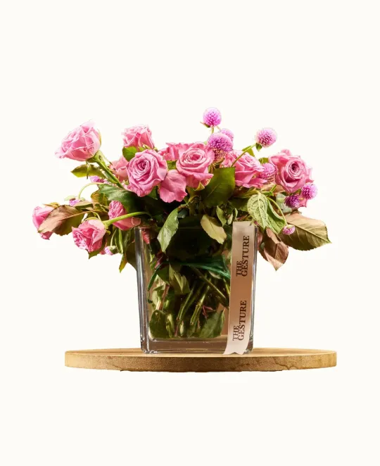 Pink floral arrangement in clear glass vase on wooden base
