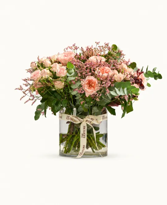 Pink and peach flower arrangement in clear glass vase with greenery