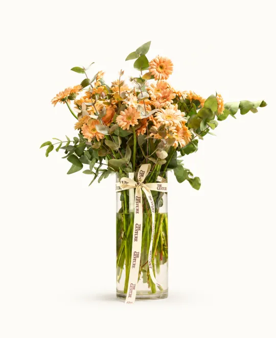 Bouquet of peach and cream roses with greenery in clear glass vase
