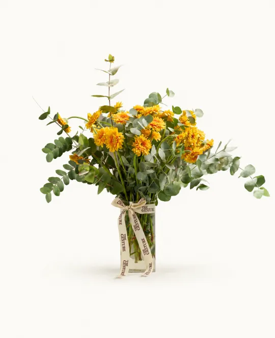 Floral arrangement with yellow and orange flowers and eucalyptus in a clear glass vase