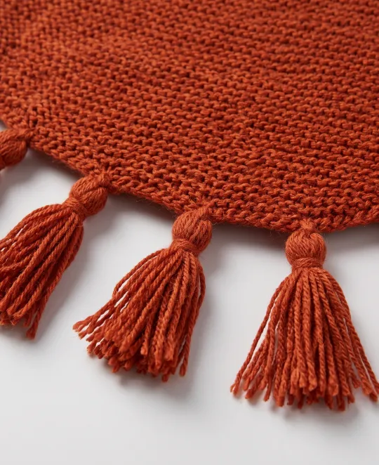 Rust-colored knitted fabric with decorative tassel trim along the edge