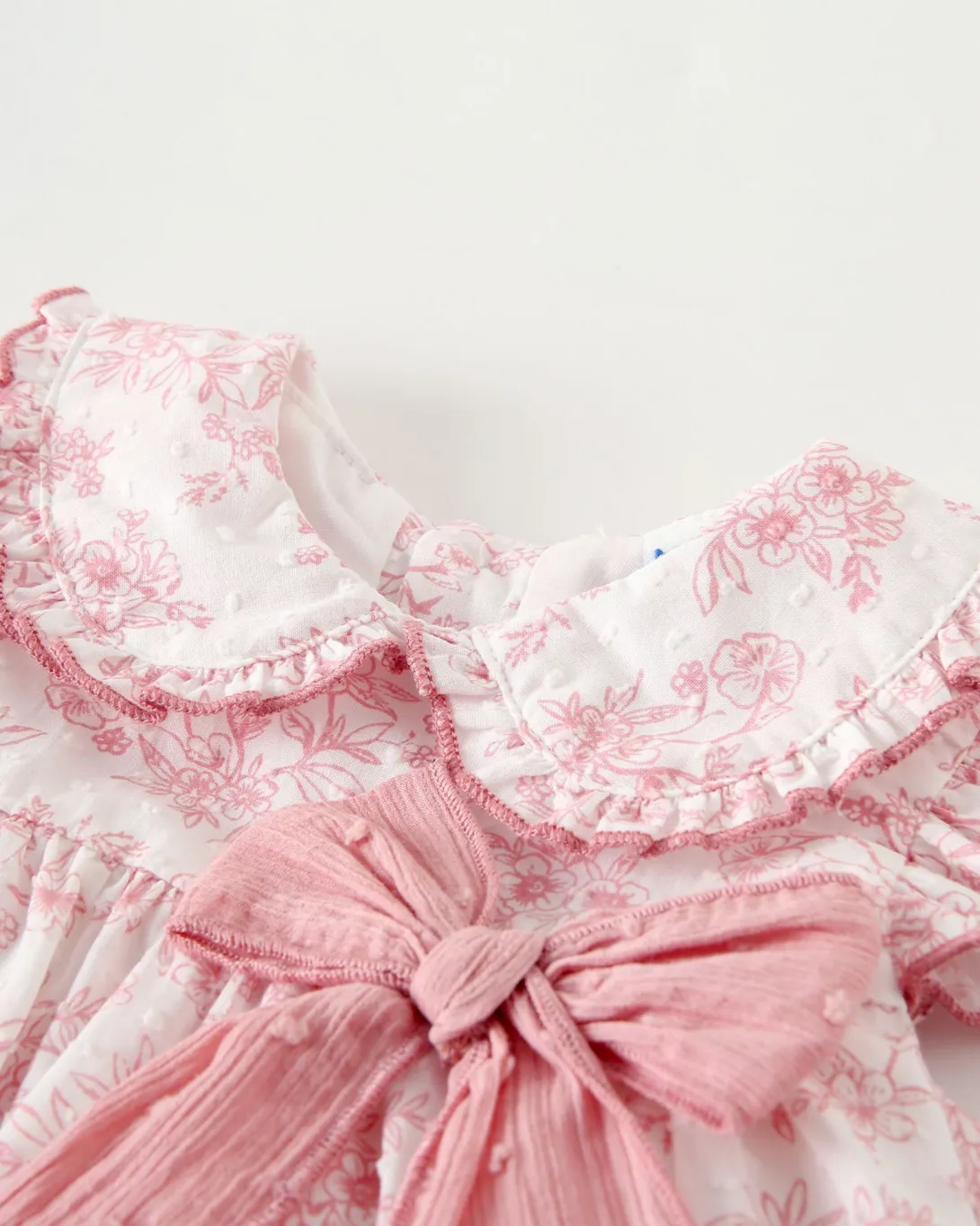 Pink children's dress with white lace collar and bow detail at waist