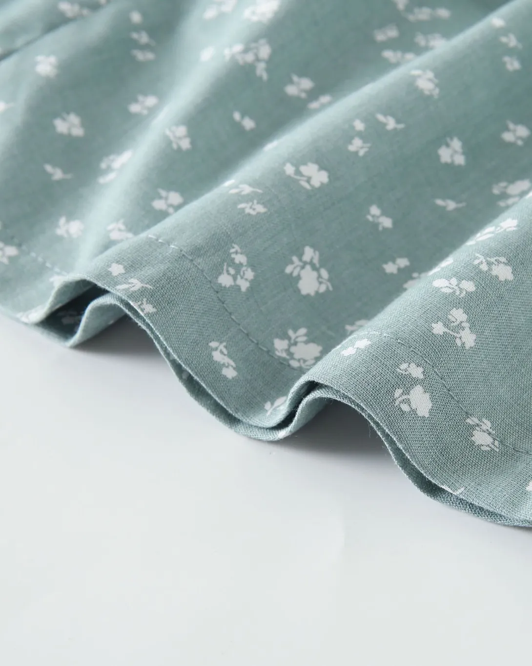 Sage green fabric with white floral print, showing quilted texture and scalloped edge