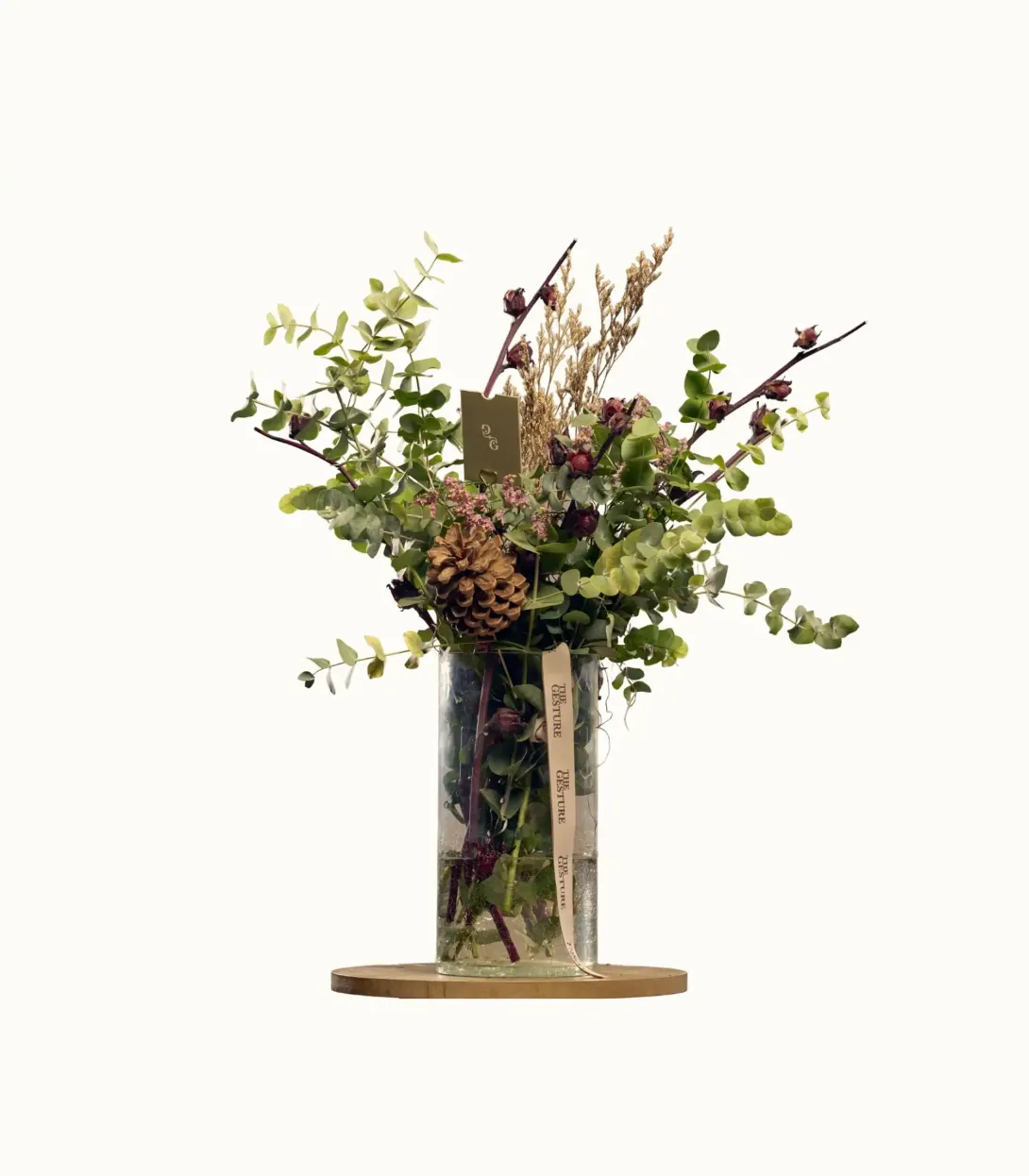 Artificial floral arrangement with greenery and branches in a clear glass vase on a wood base