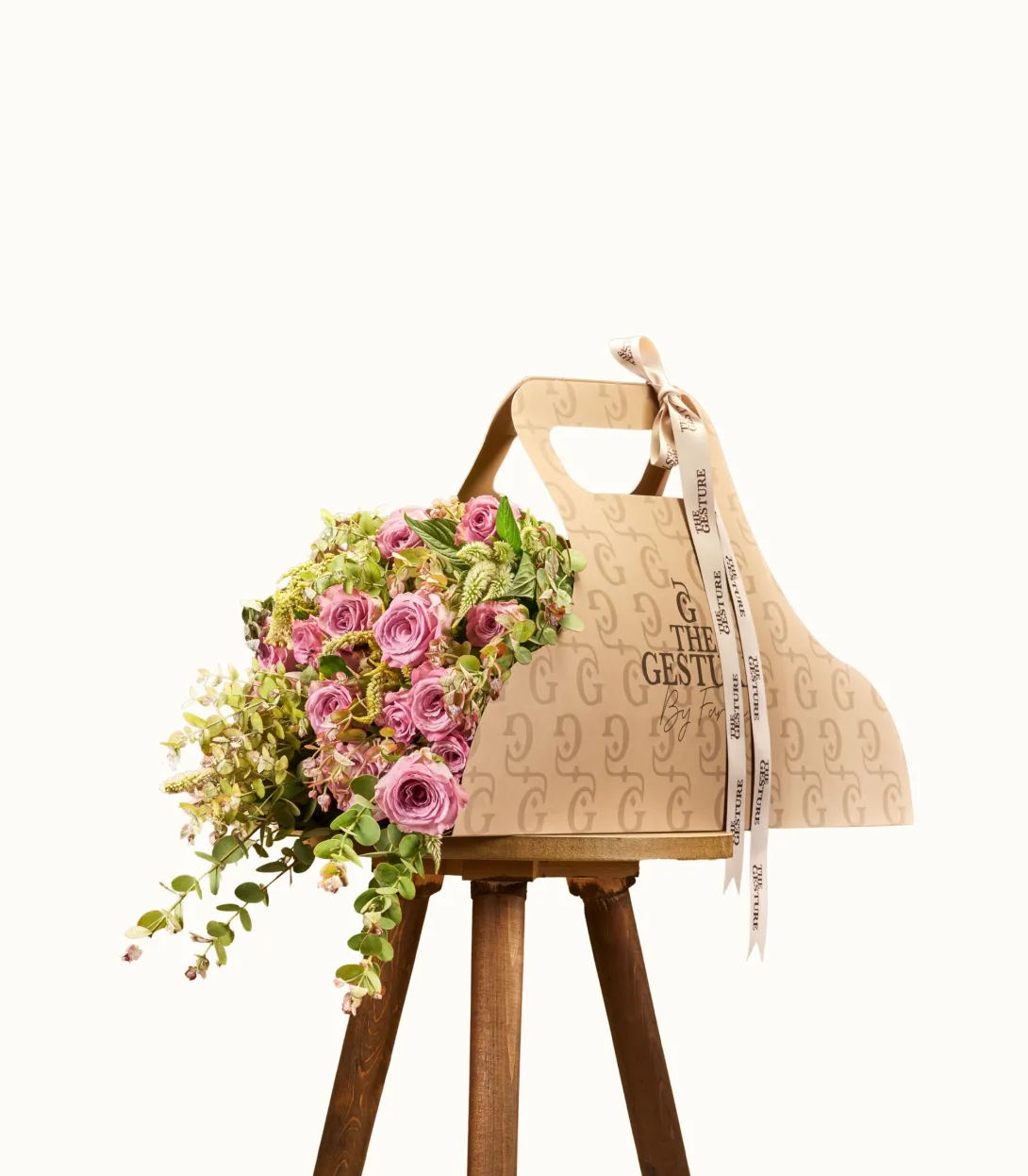 Woven straw tote bag with tassel on wooden stand, pink flowers draped over side