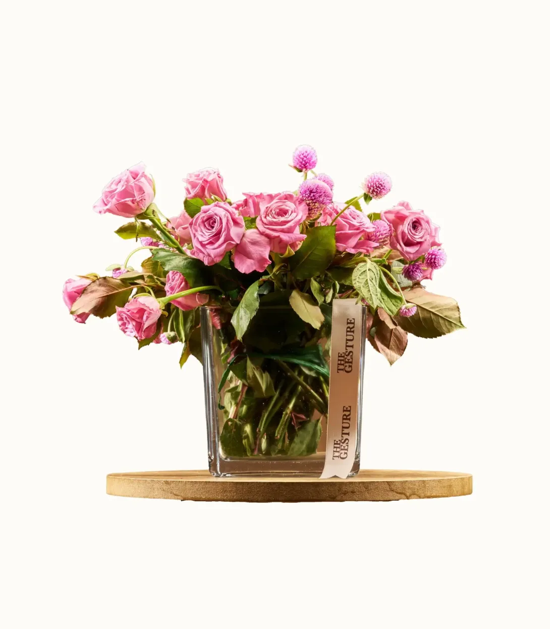 Pink floral arrangement in clear glass vase on wooden base