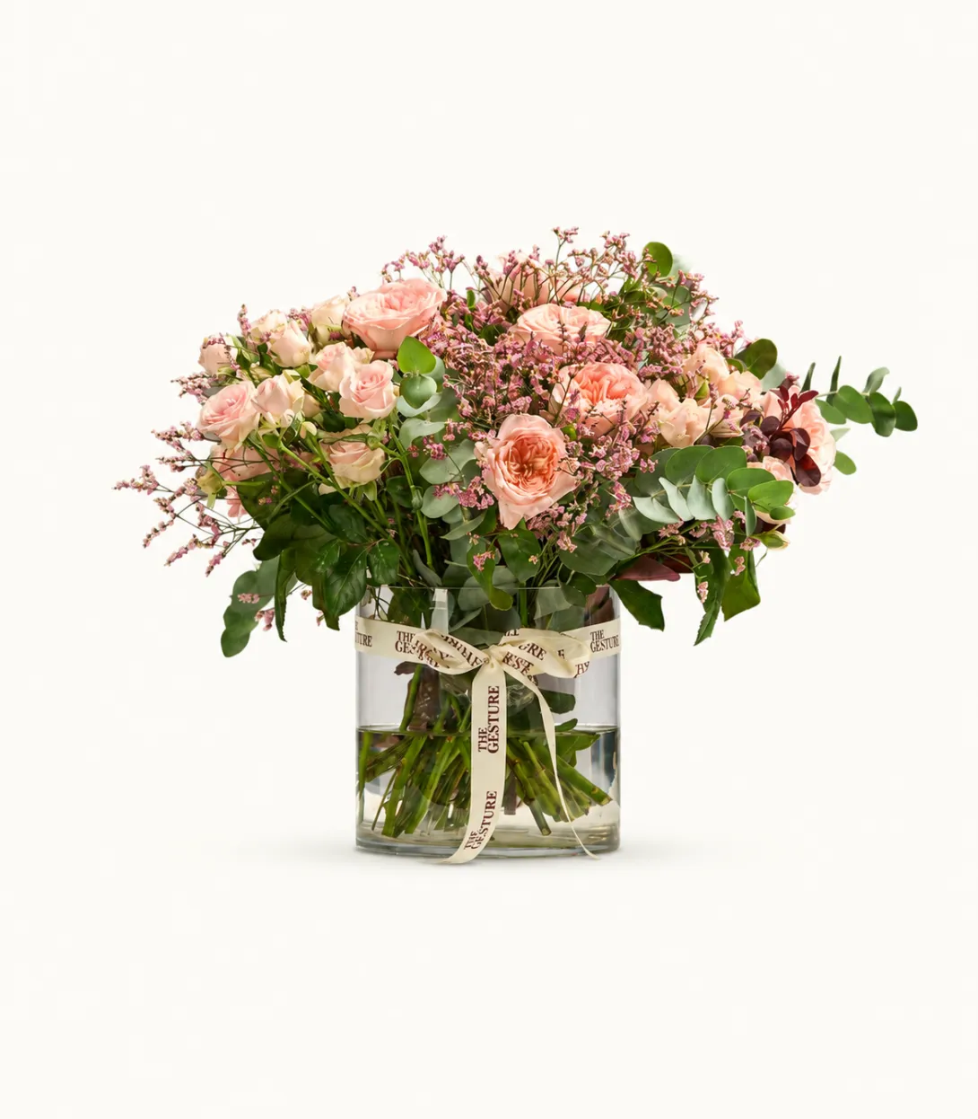 Pink and peach flower arrangement in clear glass vase with greenery