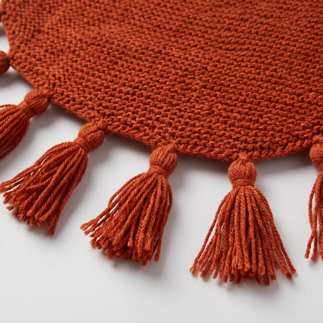 Rust-colored knitted fabric with decorative tassel trim along the edge
